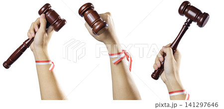 Three raised hands holding wooden judge gavels with red and white ribbons tied around their wrists, isolated on a white background. High Quality Photo Three raised hands holding wooden judge gavels with red and white ribbons tied around their wrists, isolated on a white background. High Quality Photo 141297646