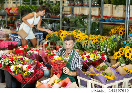 Positive male seller in apron holds designer bouquet in hands 141297650