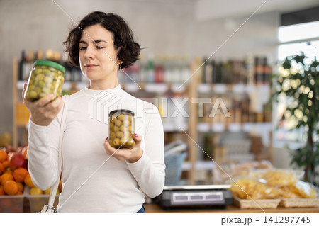 In store, woman near counter are looking at pickled green olives jar In store, woman near counter are looking at pickled green olives jar 141297745