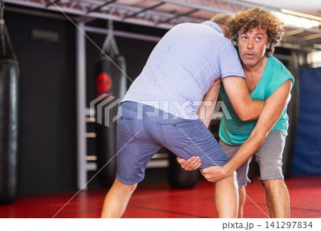 Mature man and adult man practice self-defense techniques at gym Mature man and adult man practice self-defense techniques at gym 141297834