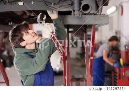 Young guy mechanic repairs underbody of car 141297854