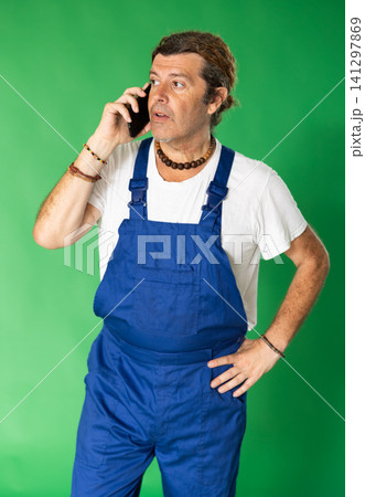 Male person wearing in blue overall is talking on phone Male person wearing in blue overall is talking on phone 141297869