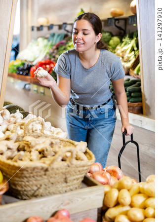 Young woman buyer chooses garlic in shop Young woman buyer chooses garlic in shop 141297910
