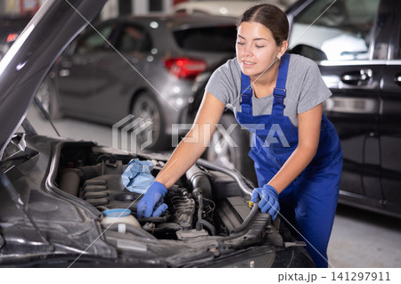 Young female mechanic repairs under hood of car Young female mechanic repairs under hood of car 141297911