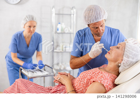 Cosmetic surgeon making lip filler injections to elderly female patient 141298006