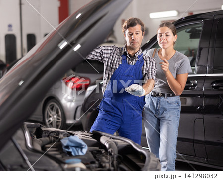 Mechanic consults woman on repairs under hood of car 141298032
