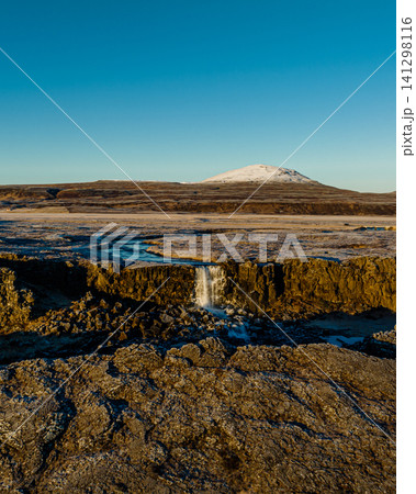 Oxarafoss waterfall in Thingvellir National Park, Iceland, surrounded by frosty winter terrain and distant snow-capped mountains. 141298116
