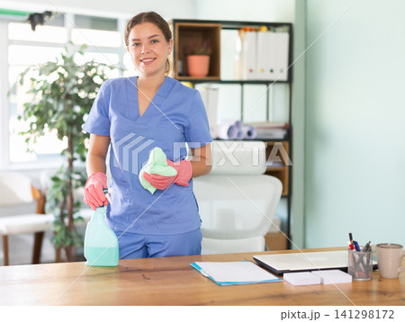 Young woman with spray and cloth standing at office desk Young woman with spray and cloth standing at office desk 141298172