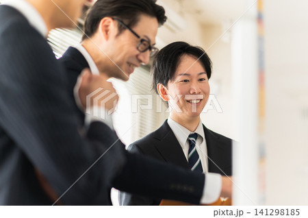 ホワイトボードを使って笑顔で打合せをする3人のスーツ姿の男性 ホワイトボードを使って笑顔で打合せをする3人のスーツ姿の男性 141298185