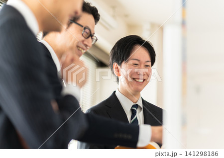ホワイトボードを使って笑顔で打合せをする3人のスーツ姿の男性 ホワイトボードを使って笑顔で打合せをする3人のスーツ姿の男性 141298186