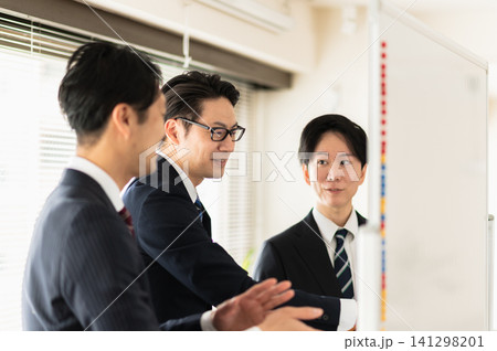 ホワイトボードを使って笑顔で打合せをする3人のスーツ姿の男性 ホワイトボードを使って笑顔で打合せをする3人のスーツ姿の男性 141298201