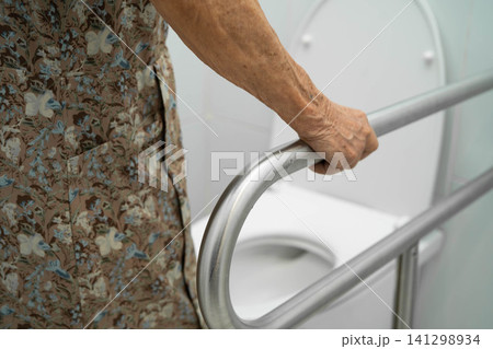 Asian elderly woman patient use toilet support rail in bathroom. Asian elderly woman patient use toilet support rail in bathroom. 141298934