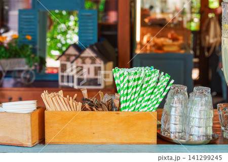 Wooden organizer with green paper straws and drink accessories at outdoor cafe bar counter Wooden organizer with green paper straws and drink accessories at outdoor cafe bar counter 141299245