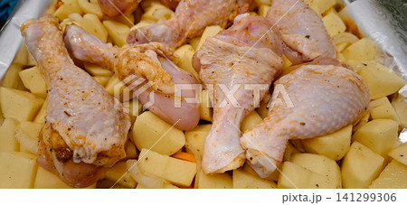 Raw chicken drumsticks and potatoes in baking tray. 141299306