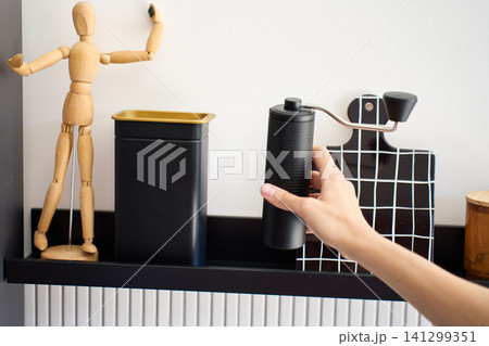 Hand picks up manual coffee grinder stored on kitchen shelf for coffee preparation Hand picks up manual coffee grinder stored on kitchen shelf for coffee preparation 141299351