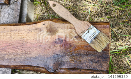 Freshly stained wooden board with paintbrush after applying protective finish. DIY woodworking, timber restoration, home renovation and wood preservation. Freshly stained wooden board with paintbrush after applying protective finish. DIY woodworking, timber restoration, home renovation and wood preservation. 141299389