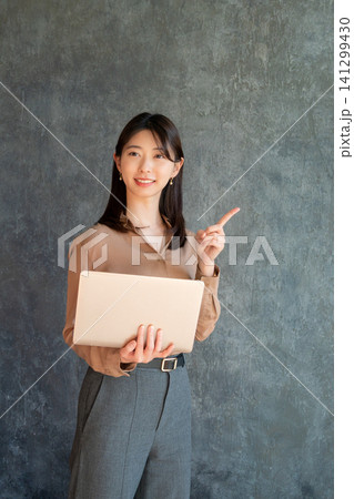 グレー背景でノートパソコンを持って指差しをする日本人女性 141299430