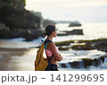 A young tourist girl with a yellow backpack meets the sunset by the ocean on the tropical island of Bali. 141299695