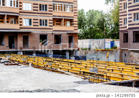 Construction site with yellow steel beams and brick apartment building under development Construction site with yellow steel beams and brick apartment building under development 141299785