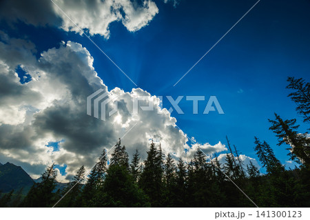 Dramatic blue sky with sun rays shining through fluffy white clouds Dramatic blue sky with sun rays shining through fluffy white clouds 141300123