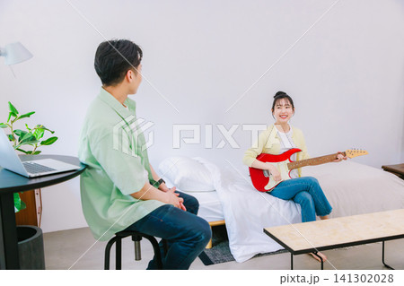 仕事をしている男性と趣味のギターを弾く女性 仕事をしている男性と趣味のギターを弾く女性 141302028