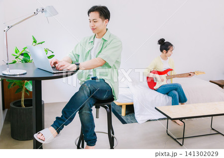 仕事をしている男性と趣味のギターを弾く女性 仕事をしている男性と趣味のギターを弾く女性 141302029