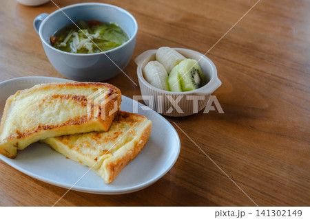 フレンチトーストとスープ、フルーツのヘルシーな朝食。木のテーブルに並べられた食卓。 フレンチトーストとスープ、フルーツのヘルシーな朝食。木のテーブルに並べられた食卓。 141302149