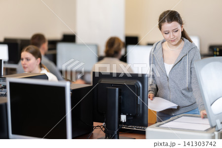Girl puts paper document into copier, makes copy using office appliances 141303742