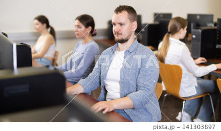 Guy student of computer courses looks at monitor screen, types on keyboard and does work 141303897