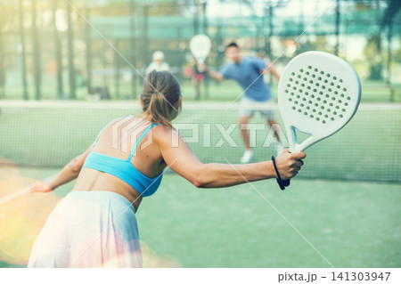 Sportive slim woman with racquet playing padel in court. View from back 141303947