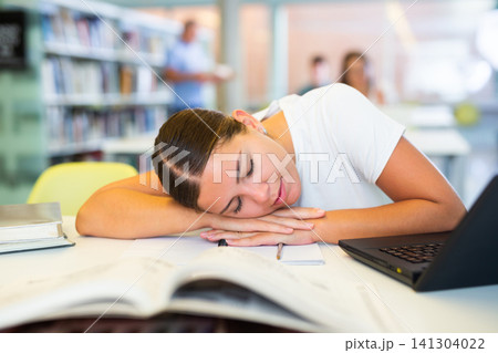 Tired female student fell asleep at the table in library 141304022