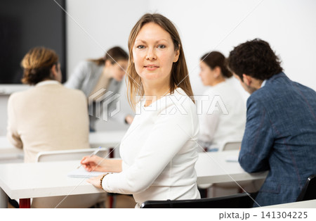 Positive middle-aged woman turning around and looking at camera during advanced training course in auditorium Positive middle-aged woman turning around and looking at camera during advanced training course in auditorium 141304225