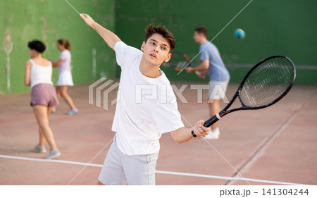 Young man serving ball during frontenis game outdoors Young man serving ball during frontenis game outdoors 141304244