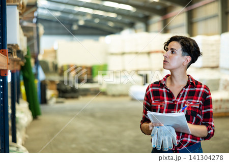 Female storekeeper checks availability of goods with documents in the building materials warehouse Female storekeeper checks availability of goods with documents in the building materials warehouse 141304278