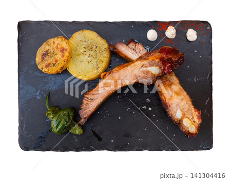 Pork ribs served with potatoes and peppers on plate 141304416