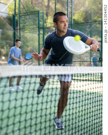 Paddle tennis player performing left-handed backhand on outdoor court 141304452