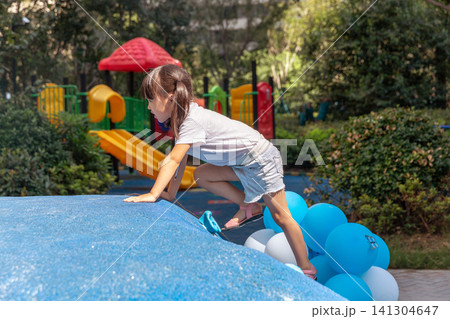A little girl is happily playing in an outdoor playground, holding many balloons in her hands. A little girl is happily playing in an outdoor playground, holding many balloons in her hands. 141304647
