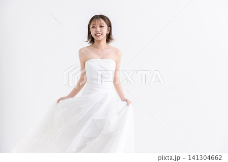 白背景の前に立ってポーズをとるウェディングドレス姿の若い女性 白背景の前に立ってポーズをとるウェディングドレス姿の若い女性 141304662