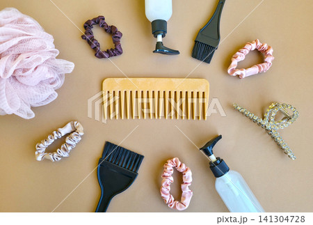 A biodegradable wooden comb sits at the center of scrunchies, hair clips and salon tools on a beige background. Concept of zero waste beauty and sustainable haircare. A biodegradable wooden comb sits at the center of scrunchies, hair clips and salon tools on a beige background. Concept of zero waste beauty and sustainable haircare. 141304728