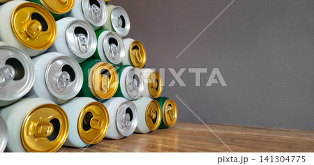 Used aluminum beverage cans stacked in a pyramid on a wood surface, plain gray wall for copy space. Concept of recycling, circular economy, and reuse of packaging. Used aluminum beverage cans stacked in a pyramid on a wood surface, plain gray wall for copy space. Concept of recycling, circular economy, and reuse of packaging. 141304775