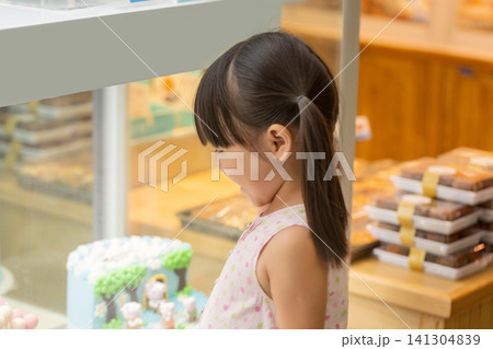 Excited little Asian girl looking at beautiful cake through glass display in a bakery shop, childhood birthday wishes. Excited little Asian girl looking at beautiful cake through glass display in a bakery shop, childhood birthday wishes. 141304839