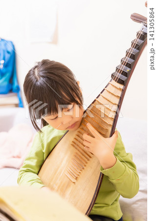 Young Chinese girl practicing Pipa traditional musical instrument on a sofa at home, creative arts and music education. Young Chinese girl practicing Pipa traditional musical instrument on a sofa at home, creative arts and music education. 141305864