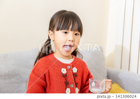 Playful elementary girl looking at camera with mouth wide open and tongue sticking straight out, holding an empty milk glass Playful elementary girl looking at camera with mouth wide open and tongue sticking straight out, holding an empty milk glass 141306024