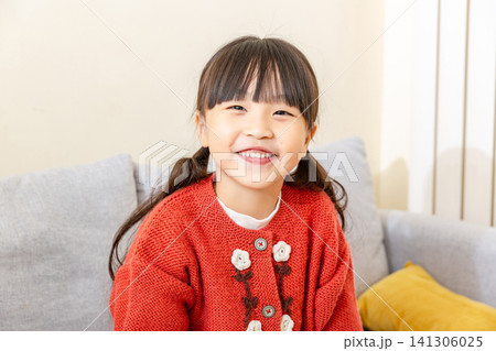 Happy and broad smile on the face of a young school-age girl sitting comfortably on a sofa at home. Happy and broad smile on the face of a young school-age girl sitting comfortably on a sofa at home. 141306025