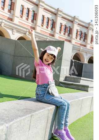 A joyful young girl raising one arm in celebration while sitting outdoors in the sun. A joyful young girl raising one arm in celebration while sitting outdoors in the sun. 141306093