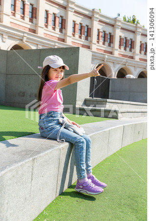 A young girl pointing into the distance while sitting on a concrete ledge outside. A young girl pointing into the distance while sitting on a concrete ledge outside. 141306094