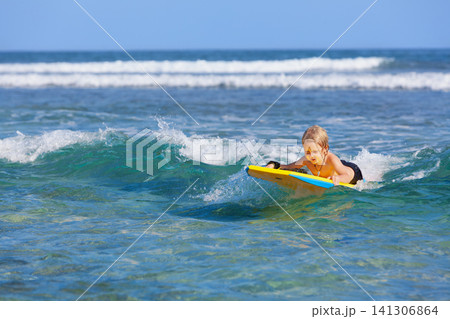 Happy young surfer boy with bodyboard have fun on beach, riding on small ocean waves. Summer adventures, active families, parents and kids lifestyle, sports activities on school holiday with kids Happy young surfer boy with bodyboard have fun on beach, riding on small ocean waves. Summer adventures, active families, parents and kids lifestyle, sports activities on school holiday with kids 141306864