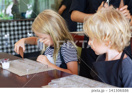 Blond girl carefully squeezes melted chocolate into molds at a workshop in Bali. A hands-on, educational activity for children traveling with family. Blond girl carefully squeezes melted chocolate into molds at a workshop in Bali. A hands-on, educational activity for children traveling with family. 141306886