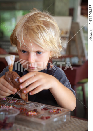 Blond boy carefully squeezes melted chocolate into molds at a workshop in Bali. A hands-on, educational activity for children traveling with family. Blond boy carefully squeezes melted chocolate into molds at a workshop in Bali. A hands-on, educational activity for children traveling with family. 141306887