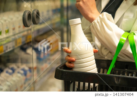A Shopper Holds a Bottle of Milk While Selecting Dairy Products from a Refrigerated Aisle in a Grocery Store. A Shopper Holds a Bottle of Milk While Selecting Dairy Products from a Refrigerated Aisle in a Grocery Store. 141307404